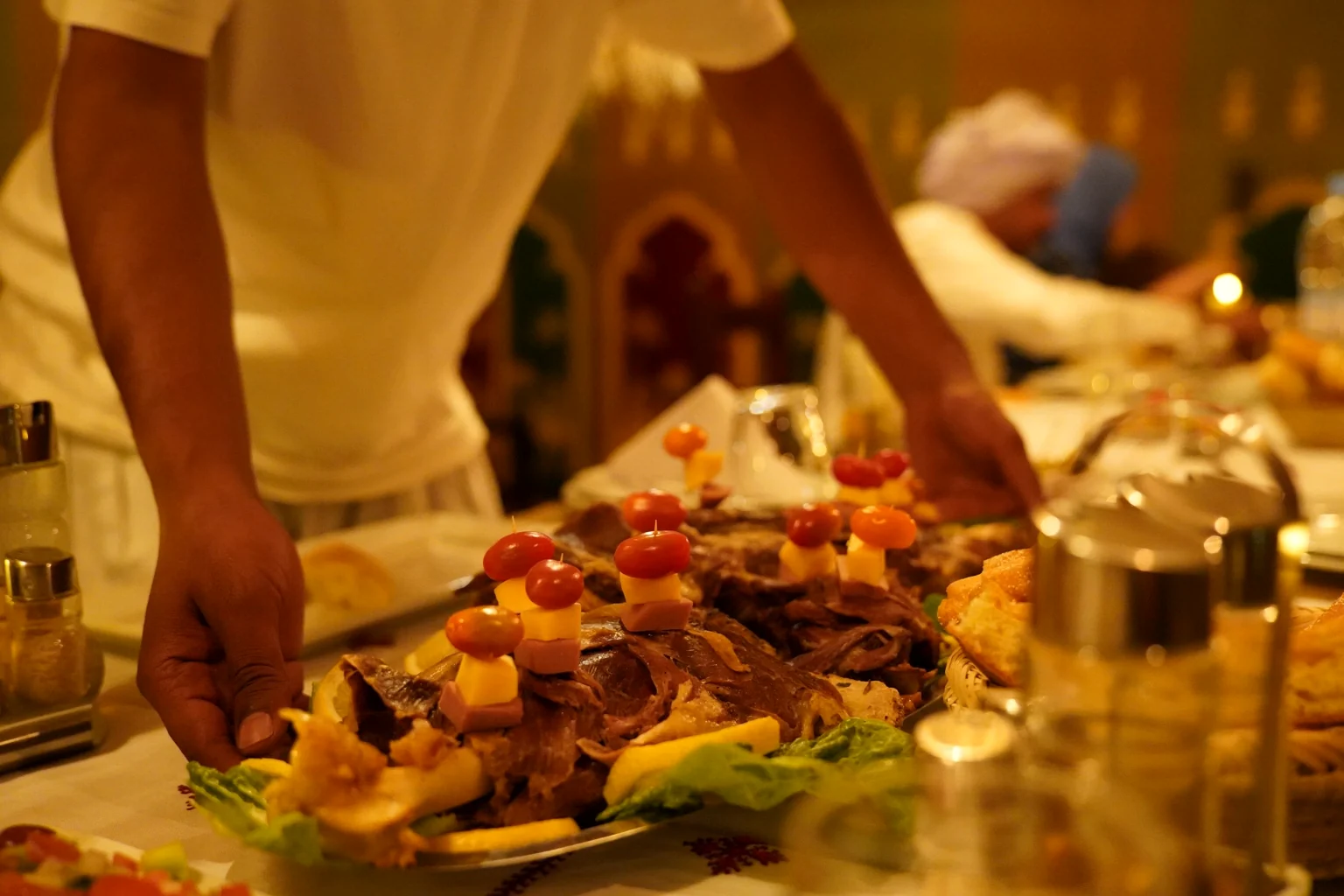 Camp staff serving a platter of Moroccan dinner dishes to guests in the candlelit dining tent