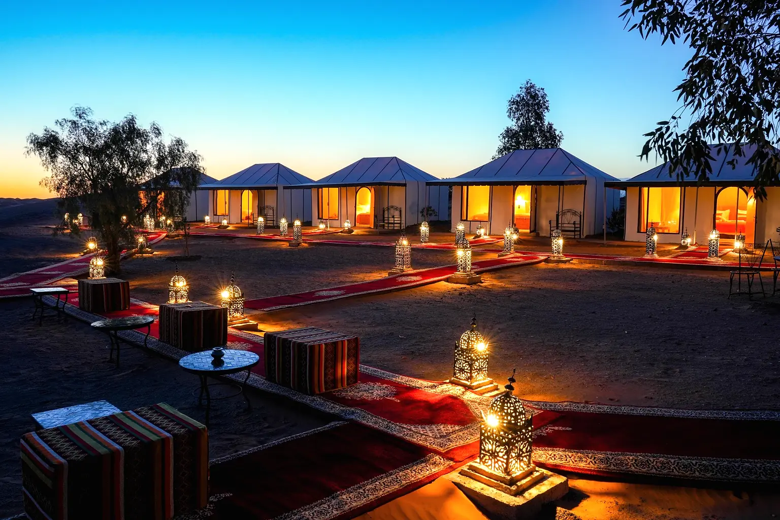 Wide night panorama of the desert camp with lanterns lining the carpet paths between the tents